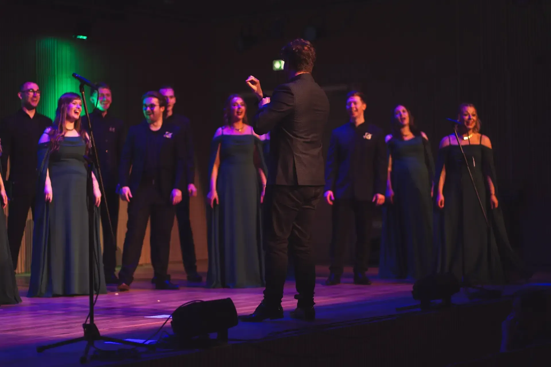 LORICA performing on stage in green gowns and black suits, led by their conductor
